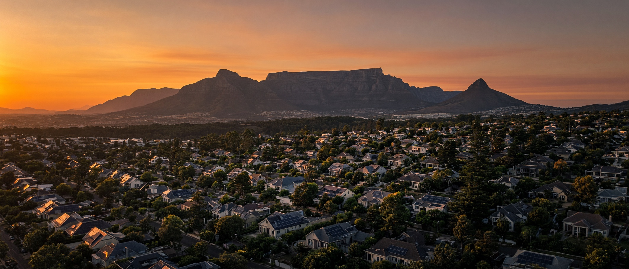 Aerial view of Cape Town suburbs with solar roofs at sunset, Table Mountain on the horizon